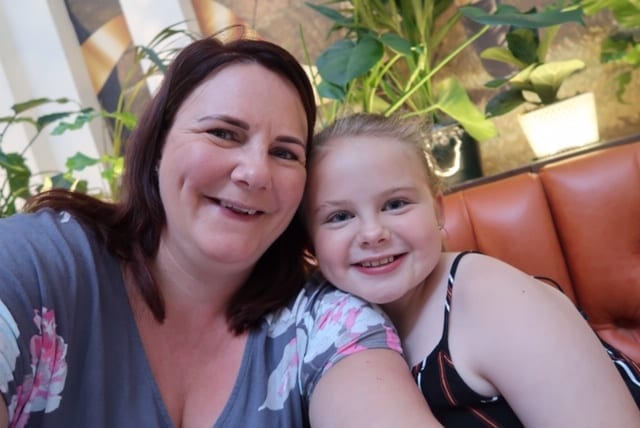 picture of Emma in a grey and pink floral t-shirt taking a selfie of her and her daughter in a black striped top