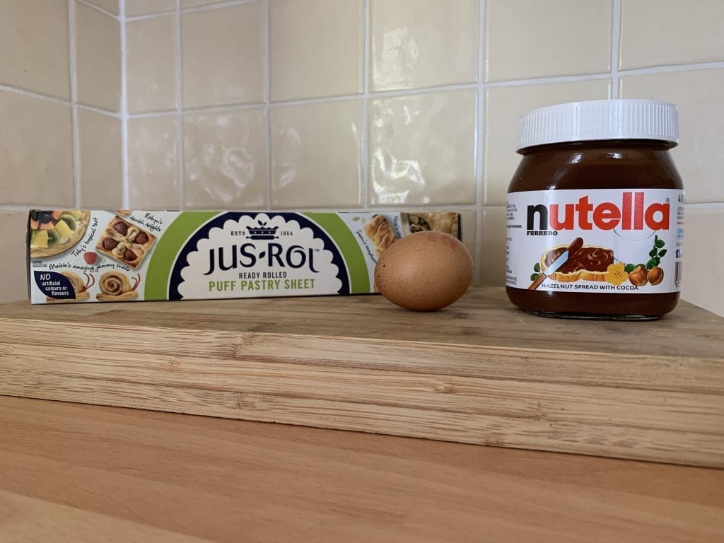 image of jus-rol puff pastry roll, an egg and a jar of Nutellas on a chopping board ready to make puff pastry with nutella
