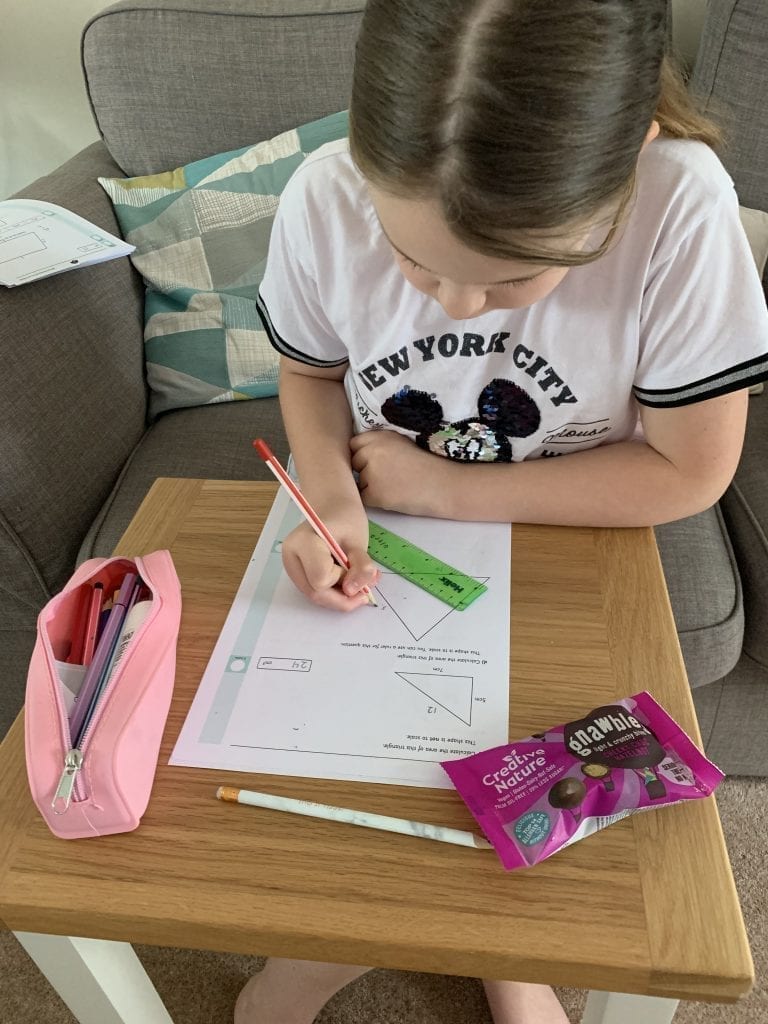 girl in white t shirt doing home learning eating gnawbles gluten free and dairy free snacks